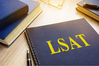 An LSAT study planner lays on a desk along with an assortment of unnamed books and a pair of glasses. Light streams in from the top of the frame.