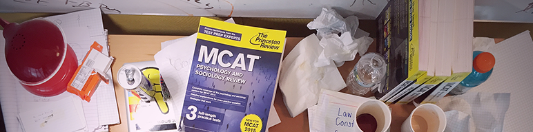 Welcome to your MCAT Product Resources this image features The Princeton Review's Psychology and Sociology Review book on a messy student's desk riddled with empty coffee cups, energy drink cans, and crumpled paper. Soon, your desk will look like this! Always nice to have something to look forward to.